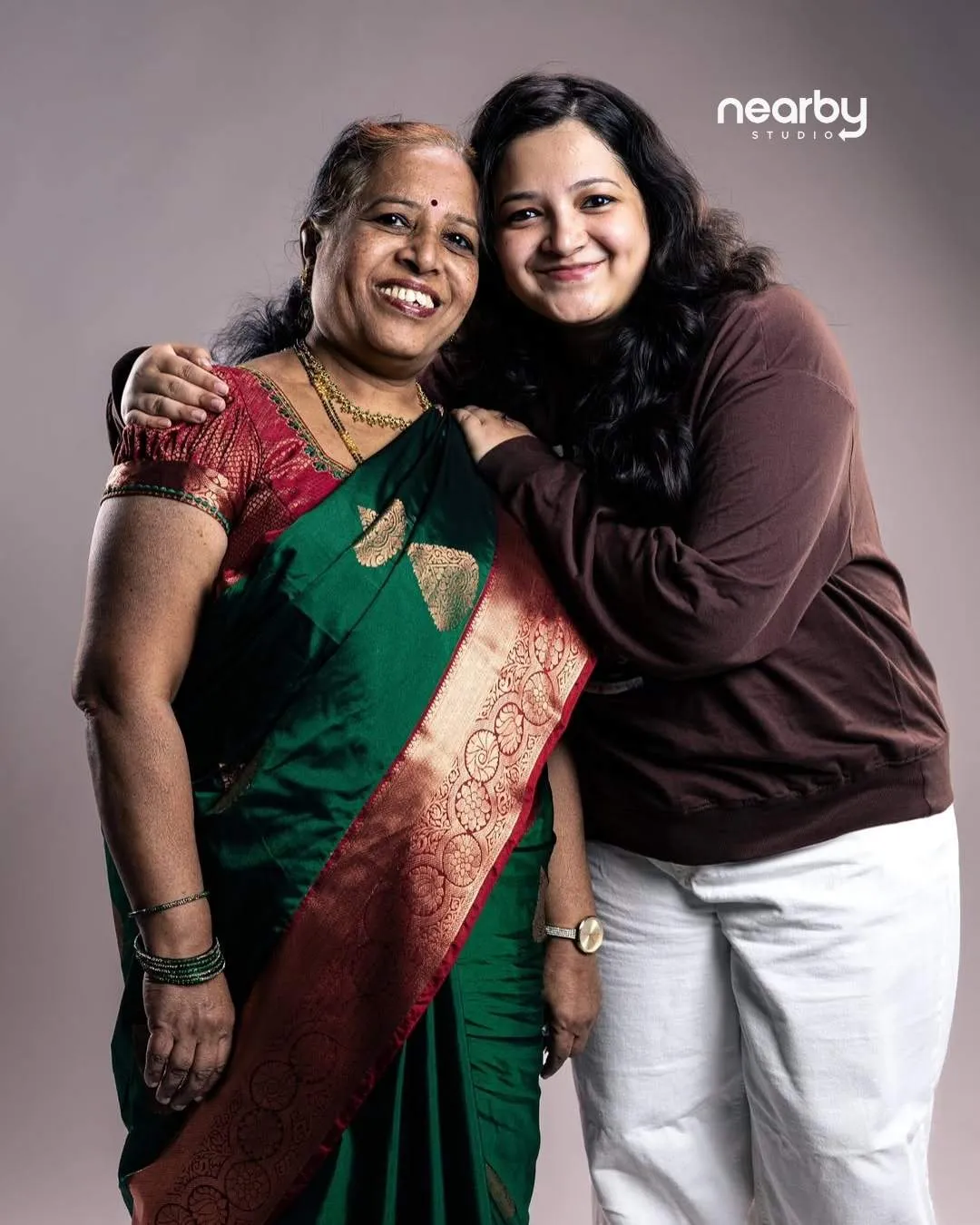 Studio portrait of a woman in a green silk saree and her daughter, lit with directional light against a grey backdrop at Nearby Studio